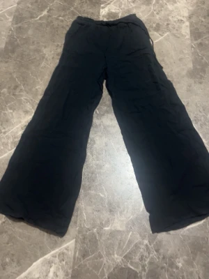 Svarta vida linnebyxor - Säljer ett par svarta linnebyxor med bred passform och resår i midjan. Byxorna har en avslappnad look och är tillverkade i ett lätt och luftigt linnematerial, perfekta för en chill och stilren outfit.