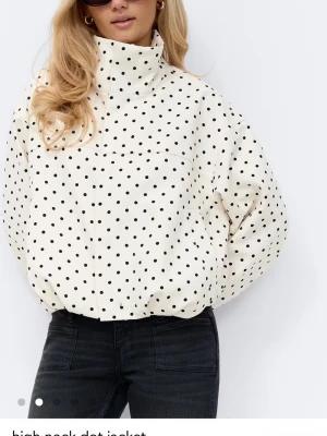 Prickig vit vindjacka med hög krage - Snygg vit vindjacka med svarta prickar och hög krage. Jackan har en loose passform och långa ärmar, perfekt för dig som vill sticka ut. Tillverkad i ett lätt material som känns bekvämt och trendigt. Slutsåld!!