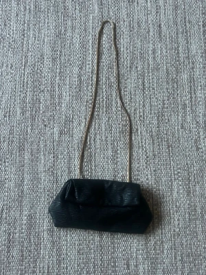 Svart liten väska med guldkedja - Stilren svart liten väska perfekt för fest eller bal. Kedjan kan justeras genom att vika in den i själva väskan. Superfin!!