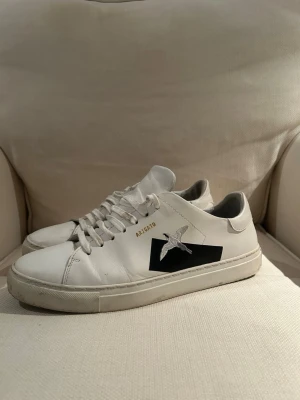 Vita sneakers från Axel Arigato - Säljer ett par vita sneakers från Axel Arigato. Använt skorna ett fåtal gånger. Skorna har svart detalj och en broderad fågel på sidan. Skorna har vita snören och diskret guldtext vid snörningen. Tillverkade i läder, perfekta för en clean och stilren look nu till sommaren! Hör av dig vid fler frågor😊