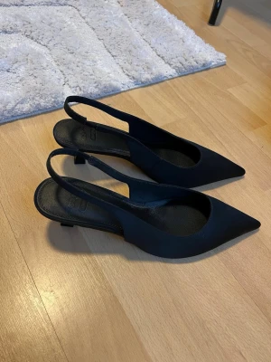 Svarta slingback pumps med låg klack - Svarta pumps med spetsig tå och slingback-rem. Skorna har låg klack och är tillverkade i ett matt material. Från ASOS, Storlek 39 och helt oanvända då de var för stora för mig!