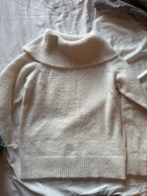 Vit stickad polotröja - Mysig vit stickad tröja med bred polokrage och ribbade detaljer vid krage, ärmslut och nederkant. Tröjan har en avslappnad passform och är tillverkad i ett mjukt, fluffigt material som känns skönt mot huden.