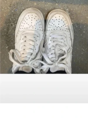 Vita sneakers - Fräscha vita Nike sneakers med klassisk låg siluett. Skorna har perforerad tå, snörning och platt sula. Tillverkade i skinn med diskret Nike-logga på hälen. Perfekta för dig som gillar clean och tidlös streetstil.