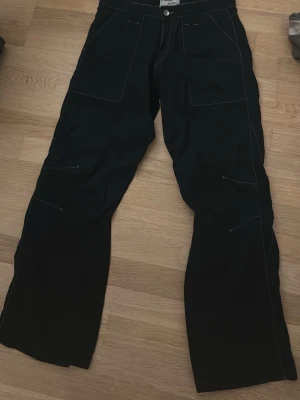 Svarta jeans från Energie - Säljer ett par svarta jeans från Energie med raka ben och kontrastsömmar. Jeansen har stora fickor framtill och coola detaljer med synliga sömmar. Perfekta för dig som gillar streetwear och en avslappnad stil.
