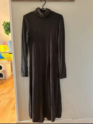 Mörkbrun långklänning med polokrage - Säljer en mörkbrun långklänning med polokrage och långa ärmar. Klänningen har en ribbad struktur framtill som ger en snygg detalj. Perfekt för dig som gillar en stilren och enkel look. Materialet känns mjukt och stretchigt.
