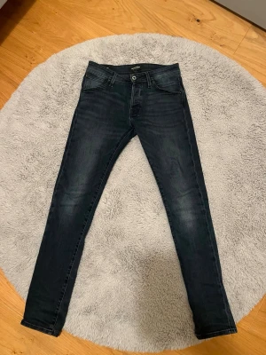 Mörkblå jeans från Jack and Jones  - Säljer ett par mörkblå skinny jeans från Jack and Jones med klassisk femficksdesign och lätt slitna detaljer. Jeansen har normal midja, smal passform och är tillverkade i stretchigt denimtyg för extra komfort. Perfekta för en trendig och avslappnad look. Modellen heter Slim Glenn, är i storlek W28 L32, väldigt bra skick!