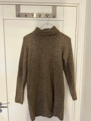 Beige stickad polotröja från Pieces - Mysig brun stickad polotröja från Pieces. Tröjan är lång, har långa ärmar och en hög polokrage. Perfekt för en mysig outfit. 😍Materialet känns mjukt och värmande.