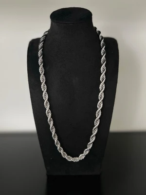 Cordell Halsband 7mm - Säljer ett stilrent halsband med tjock, tvinnad kedja i silverfärg. Halsbandet har en chunky look och glänsande finish som ger en modern vibe. Perfekt för dig som vill ha ett statement piece till din outfit. Materialet ser ut att vara metall.