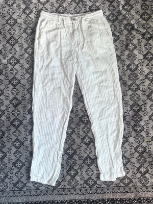 Vita linnebyxor med resårmidja - Säljer ett par vita linnebyxor med avslappnad passform och resår i midjan. Byxorna har fickor fram och bak samt stängs med knapp och dragkedja. Perfekta för en chill och luftig stil under varma dagar. Dessa kommer sitta super inför sommaren som snart är här. Ny pris:899kr   Mitt pris: 499