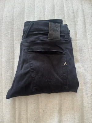 Svarta slim jeans från Replay - Snygga svarta slim fit jeans från Replay med klassisk femficksdesign och detaljer som Replay-logga på bakfickan och läderpatch i midjan. Jeansen är tillverkade i stretchigt bomullsmaterial för skön passform och har dragkedjegylf.