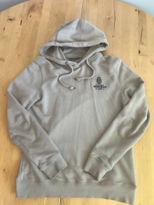 Beige hoodie från Morris - Snygg beige hoodie från Morris med broderad logga och emblem på bröstet. Tröjan har huva med dragsko och ribbade muddar vid ärmslut och nederkant. Perfekt för en avslappnad och stilren look. Nypris ligger på ca 1700 kr. Vid intresse kan även pris diskuteras;)