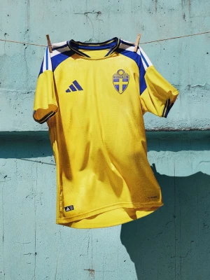 Svensk landslagströja Adidas gul - Gul svensk landslagströja från Adidas med blå detaljer och vita inslag på axlarna. Tröjan har broderad svensk landslagssköld på bröstet och Adidas-logga. Tillverkad i lätt och ventilerande material, perfekt för fotboll eller träning. Finns med gyköres och utan, finns i många storlekar 