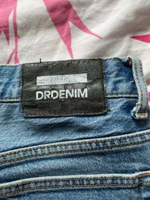 Blå raka jeans från Dr Denim - Säljer ett par klassiska blå jeans från Dr Denim med raka ben och hög midja. Jeansen har två bakfickor och är gjorda i ett mjukt denimtyg. Perfekta till vardags för en avslappnad och trendig look.