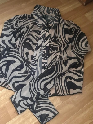 Zebramönstrad transparent skjorta - Säljer en långärmad skjorta med svart och beigt zebramönster. Skjortan är transparent och har klassisk krage samt knäppning framtill. 