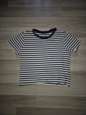 Randig croppad t-shirt från Etrel - Säljer en croppad t-shirt från Etrel med svartvita horisontella ränder. T-shirten har korta ärmar och en svart ribbad krage. Perfekt till jeans eller kjol för en avslappnad look.
