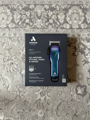 Andis Envy Li sladdlös hårtrimmer - Säljer en Andis Envy Li hårtrimmer som funkar både med och utan sladd. Trimmern har ett justerbart blad och levereras med flera distanskammar. Färgen är metallic blå/lila och designen är ergonomisk och lättviktig. Perfekt för styling, fades och tapers. Köpt för: 1900kr