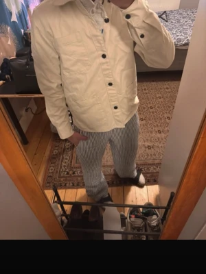 Beige overshirt från Dressman - Stilren beige overshirt med stora svarta knappar och tre rejäla fickor framtill. Rak passform och klassisk krage, perfekt för lager-på-lager. Tillverkad i ett kraftigare bomullstyg som ger en clean och modern look.