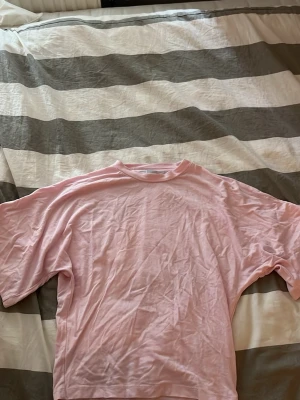Ljusrosa oversized t-shirt - En enkel och stilren ljusrosa t-shirt i oversized modell. T-shirten har rund halsringning och korta ärmar. Perfekt för en avslappnad och trendig look. Tillverkad i mjuk bomull för maximal komfort.