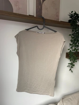 Beige ärmlös topp i bomull - En enkel och stilren beige topp i mjuk bomull. Modellen är ärmlös med rund halsringning och har en rak passform som sitter snyggt på kroppen. Perfekt att matcha med jeans eller kjol för en clean look.