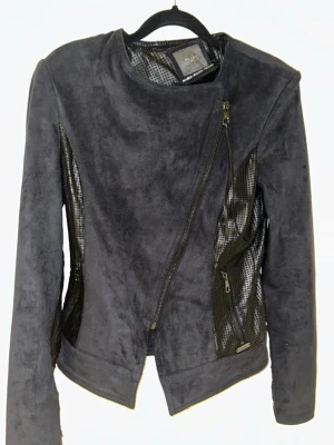 Svart skinnjacka från Guess - Snygg svart jacka från Guess med asymmetrisk dragkedja och coola meshdetaljer på sidorna. Jackan har en modern, figurnära passform och diskreta metalliska dragkedjor. Perfekt för dig som vill ha en edgy look.