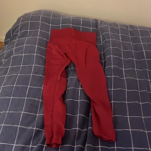 Mörkröda leggings med hög midja - Säljer ett par mörkröda leggings med hög midja och smal passform. De är stretchiga och sitter tight längs benen, perfekta för en trendig och bekväm look. Materialet känns mjukt och följsamt mot huden. Inga synliga fickor eller detaljer.