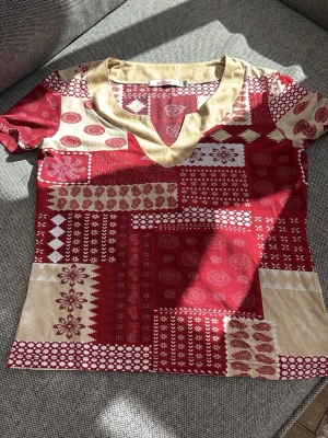 Y2K/vintage Röd och beige topp från s.Oliver - Unik topp från s.Oliver i rött och beige med patchwork-inspirerat mönster och v-ringning. Toppen har korta ärmar och detaljerade tryck med blommor och geometriska former. Perfekt för dig som gillar färg och mönster!