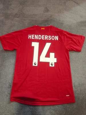 Liverpool Hemmatröja | 2019-20 | Henderson - Liverpools Hemmatröja från Premier League vinnar säsongen 2019-2020. Henderson, nr 14 på ryggen. Stadium/fan edition. Ny & oanvänd. Storlek large. Tröjan är en replika i utmärkt kvalitet. Skickas 1-3 dagar efter mottagen betalning. Har du frågor/funderingar är det bara att höra av dig! :)