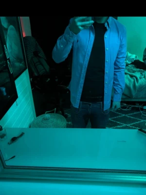 Blå skjorta från Ralph Lauren - Klassisk blå skjorta från Ralph Lauren med den ikoniska broderade loggan på bröstet. Skjortan har knappar framtill och lång ärm. Tillverkad i bomull för en bekväm känsla och snygg passform. Använd en gång.