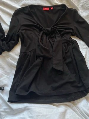 Svart topp med knyt  - Svart långärmad topp från kidsbrandstore med v-ringning och snygg knytning framtill. Toppen har en lös passform nedtill och är tillverkad i mjukt bomullsmaterial och utsvängd arm.