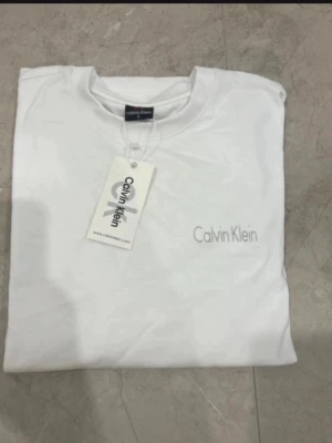 Vit Calvin Klein t-shirt i bomull - Snygg vit t-shirt från Calvin Klein med logga tryckt både framtill och på bröstet. Klassisk rund hals och korta ärmar. Tillverkad i mjuk bomull som känns skön mot huden. Perfekt till jeans eller shorts för en clean och stilren look.