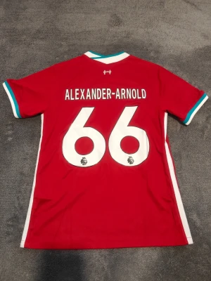 Liverpool matchtröja | 2020-21 | Trent Alexander-Arnold - Liverpools Hemmatröja från säsongen 2020-21. Alexander-Arnold, nr 66 på ryggen. Stadium/fan edition. Ny & oanvänd. Storlek large. Tröjan är en replika i utmärkt kvalitet. Skickas 1-3 dagar efter mottagen betalning. Har du frågor/funderingar är det bara att höra av dig! :)
