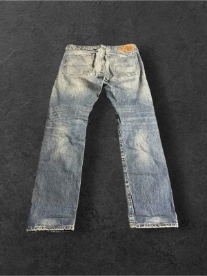 Denim & Supply  blå slitna raka jeans | W32 L32 - Säljer ett par klassiska blå RLDS med rak passform och slitningar, inklusive ett hål på vänster knä. Jeansen har fem fickor, läderpatch bak i midjan och tydliga slitdetaljer för en vintage look. Perfekta för dig som gillar en avslappnad och trendig stil.
