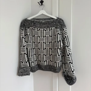 Svartvit stickad tröja med grafiskt mönster - Säljer en stickad tröja i svart och vitt med ett coolt grafiskt rutmönster. Tröjan har bred ribbstickad mudd vid ärmslut och nederkant samt en lös, avslappnad passform. 