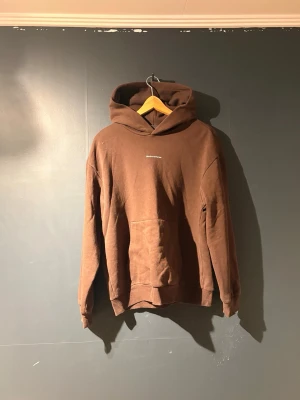 Brun hoodie med tryck på ryggen - Snygg brun hoodie från Samsøe Samsøe med liten vit text på bröstet och ett stort tryck med naturmotiv på ryggen. Hoodien har huva och magficka, samt ribbade muddar vid ärmslut och nederkant. Perfekt för en chill och stilren look.