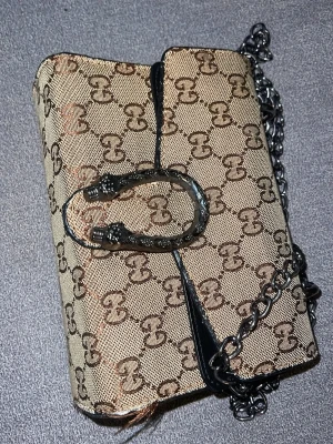 Axelväska - Trendig och Snygg( ej äkta)   Gucciväskq i beige canvas med klassiskt GG-mönster och detaljer i svart läder. Fint skick 