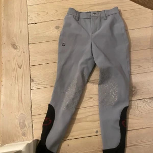 Grå ridbyxor från cavalleria Toscana  - Snygga grå ridbyxor med silikongrepp på insidan av benen för extra fäste. Byxorna har en knapp och dragkedja framtill samt svarta detaljer vid bensluten. Perfekta för ridning och ger en stilren look i stallet. Med några så hål vid knät🤗