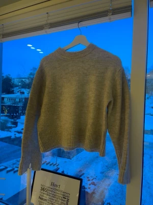 Beige stickad tröja Gina Tricot - Mysig beige stickad tröja från Gina Tricot med rund halsringning och ribbade muddar vid ärmslut och nederkant. Tröjan har en enkel, klassisk design och är perfekt för lager på lager under kyliga dagar.