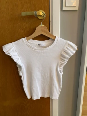 Vit ribbad topp med volangärmar Zara - Superfin topp från Zara med volang ärm och ribbat tyg. Den är i storlek S men den är lite kortare i modellen. Den är andvänd en/två gånger.