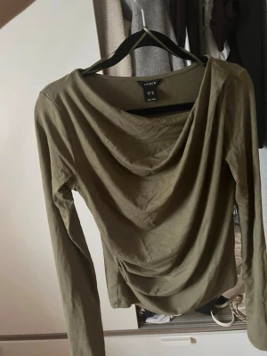 Olivgrön topp från Lindex - Olivgrön långarmad topp med hängande framsida. Använd ett fåtal gånger. hör av er vid frågor!❤️