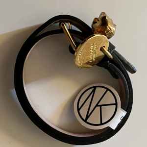 Alexander McQueen läder armband - Svart smalt läder armband i skinn från Alexander McQueen med guldfärgat spänne och detaljer.  läder armbandet har en ikonisk dödskalleberlock och en rund medaljong med ingraverad text. Perfekt accessoar för att lyfta din outfit med en edgy touch. original pris ligger på cirka 1900 - 1500kr.