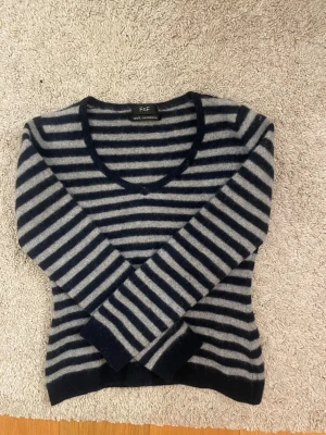 Randig kashmirtröja från F&F - Mysig långärmad tröja från F&F i 100% kashmir. Tröjan har marinblå och gråa ränder, v-ringad hals och ribbade muddar. Perfekt för dig som gillar klassisk stil med en twist.
