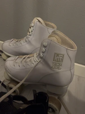 Vita rullskridskor från School - Säljer ett par klassiska vita rullskridskor från School med högt skaft och snörning hela vägen upp. De har robusta hjul och är tillverkade i konstläder. Perfekta för dig som vill åka retro på gatan eller i hallen.