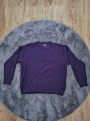 Lila stickad tröja med rund hals - En stilren lila stickad tröja med rund halsringning och långa ärmar. Tröjan har en enkel, klassisk design utan mönster och ribbstickade muddar vid ärmslut och nederkant. Perfekt för dig som gillar en clean och avslappnad look.