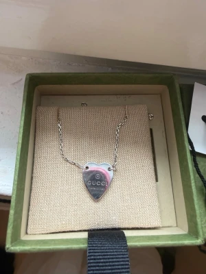 Gucci halsband med hjärta i silver - Säljer ett snyggt halsband från Gucci med ett hjärtformat hänge i silver. Kedjan är tunn och elegant, och hänget har Gucci-loggan ingraverad. Kommer i originalask med etikett. Perfekt accessoar för dig som gillar stilrena smycken. Köptes på Vinted i somras med artikelverfiering!