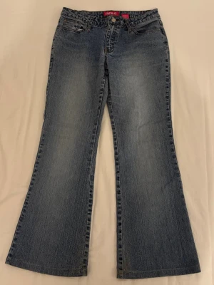 Blå Zana Di Jeans - Blå utsvängda jeans med låg midja och söta detaljer på bakfickorna från zana di. Inga synliga defekter. OBS har sytt upp jeansen så håll koll på innerbenslängden. MIDJEMÅTT: 38cm INNERBENSLÄNGD: 68cm