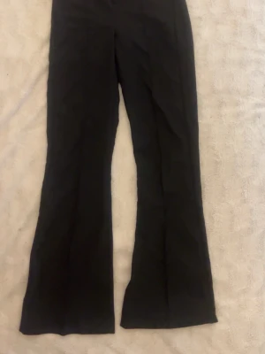 Svarta kostymbyxor från Gina Tricot - säljer ett par svarta kostymbyxor från Gina Tricot i storlek XXS. Byxorna har utsvängda ben, medel hög midja och stängs med dragkedja och knapp framtill. Sömnen nere vid vänstra benet är öppen går enkelt att laga men inte synligt.