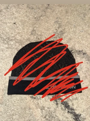 Svart mössa med grå rand - Säljer en svart mössa med en grå rand runt uppviket. Klassisk modell som passar perfekt till höst och vinter. Materialet ser ut att vara stickat och mössan har en enkel, stilren design.