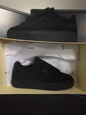 Svarta sneakers från Axel Arigato - Stilrena helsvarta sneakers från Axel Arigato i mocka med diskret logga på sidan. Klassisk låg modell med svart sula och minimalistisk design. Perfekta för dig som gillar en clean och modern look.