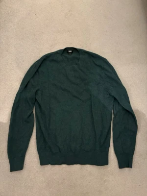 Mörkgrön cashmere tröja från Uniqlo - Mysig mörkgrön cashmere tröja från Uniqlo i storlek M. Tröjan har rund halsringning, långa ärmar och ribbade muddar vid ärmslut och nederkant. Perfekt för lager på lager och enkel att matcha med jeans eller kjol.