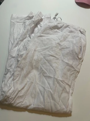 Vita linnebyxor med dragsko - Säljer ett par vita linnebyxor med avslappnad passform och dragsko i midjan. Byxorna har sidofickor och är tillverkade i ett lätt och luftigt linnematerial, perfekta för varma dagar. Stilrena och enkla att matcha med olika toppar.